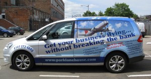 Image shows a silver Ford Galaxy people-carrier with vehicle livery by Adamson Design. In shades of blue, the design uses an aeroplane graphic to advertise virtual office services with the slogan: "Get your business flying… without breaking the bank."