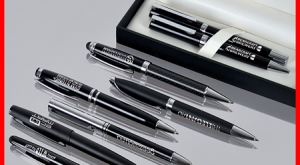Photo of eight black metal pens engraved with logos and contact details, with the engraving showing silver out of black.