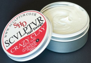 Photo shows a circular silver tin of mens hair wax opened, the wax is off-white. The lid has a bold red-and-black design called Crazy Clay, part of the Sculptur range.