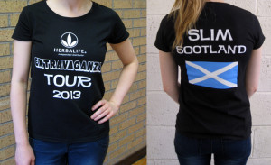 Front and back views of the Herbalife-Slim Scotland T-shirt being modelled. It is a black lady-cut T-shirt with white design showing (front) the Herbalife logo and Extravaganza Tour 2013 and (back) Slim Scotland and the Saltire, which is in white-on-blue.