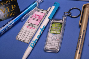 A close-up photo of Promotional Goods showing the branding details on a VIP membership card, three pens and two mobile-phone-shaped keyrings.