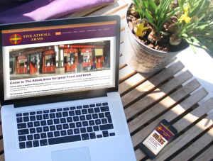Mockup photo of "The Atholl Arms" website design on MacBook Pro and iPhone on a café table.