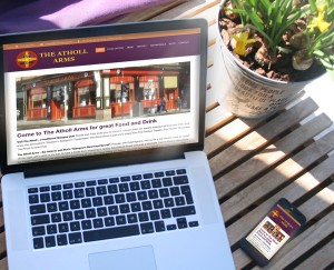 Mockup photo of "The Atholl Arms" website design on MacBook Pro and iPhone on a café table.