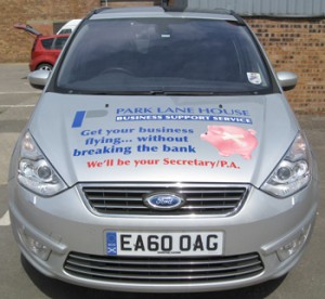 Front view of vehicle wrap graphics on a silver Ford Galaxy. This view shows the bonnet with text, logo and a broken-piggybank image symbolising "without breaking the bank", all promoting a business support service in Glasgow.