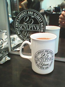 Picture shows a white mug branded with the black-white Sculptur 25 Years Logo in front of one of the mirrors in the hair salon, which is similarly branded with a logo-sticker.