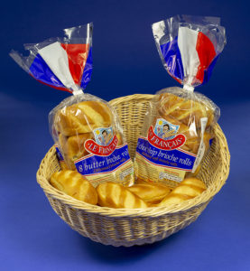 The photo shows two packs of French Brioche Rolls in their transparent packaging, sitting in a wicker basket. The packs are branded LE FRANCAIS and are decorated in red, white and blue, with the ‘tail’ of each pack simulating the French flag. There are two types of pack – Butter Brioche and Choc-Chip.