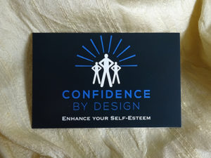 The picture is of a black business card which features the new brand identity for Confidence by Design.